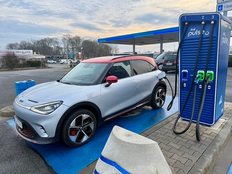 Une voiture électrique Smart #1 Brabus se charge à une station sous un ciel nuageux.