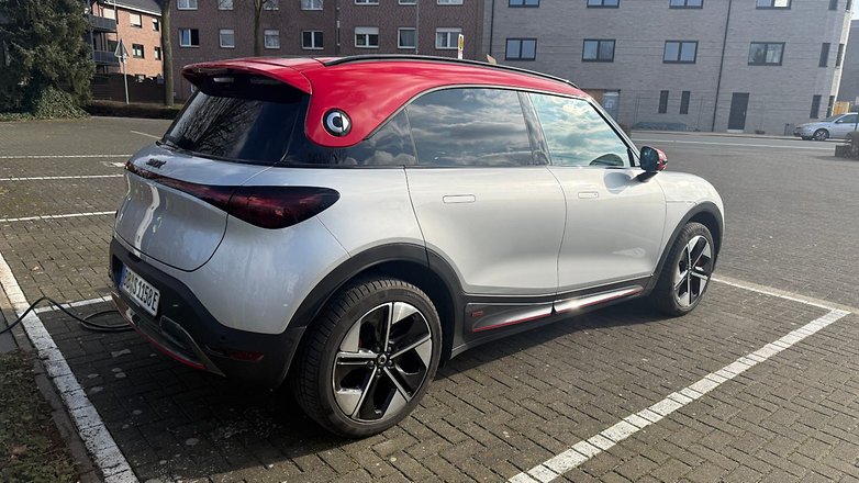 Une Smart #1 Brabus garée, avec une carrosserie argentée et un toit rouge, dans une zone résidentielle.