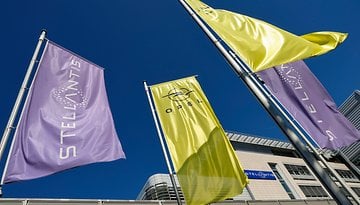 Fahnen von Stellantis und Opel wehen vor einem klaren blauen Himmel an einem Unternehmensstandort.