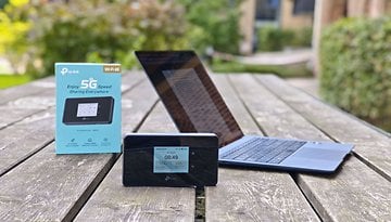 TP-Link M8550 mobiler Hotspot mit Display, Box und Laptop auf einem Holztisch im Freien.