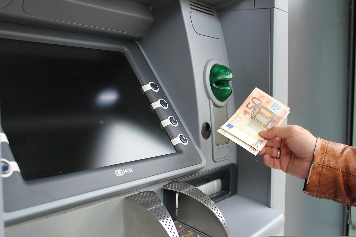 Una persona que usa un cajero automático para retirar efectivo, sosteniendo un billete de 50 euros.