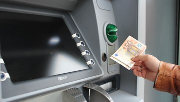 A person using an ATM to withdraw cash, holding a 50 euro banknote.