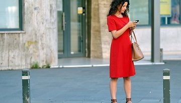 Eine Frau im roten Kleid steht auf dem Bürgersteig und schaut auf ihr Handy