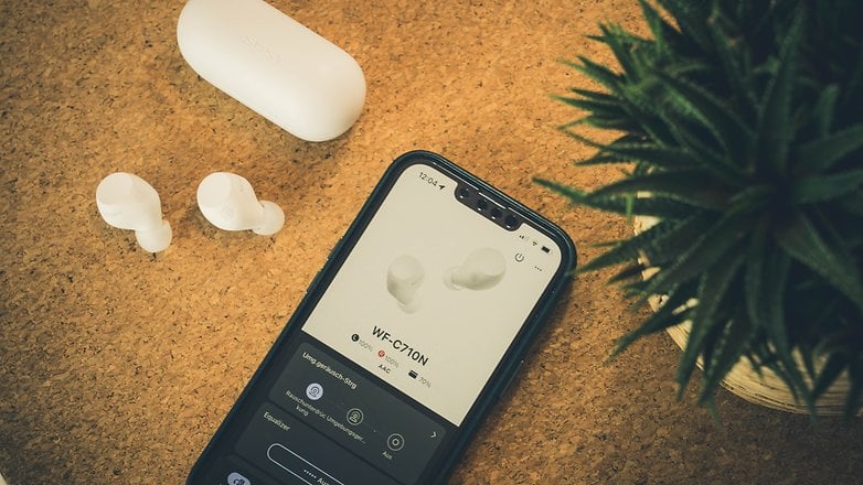 Fones de ouvido sem fio brancos da Sony com estojo de carregamento e smartphone exibindo a interface WF-C710N. Fones de ouvido sem fio brancos da Sony com estojo de carregamento e smartphone exibindo a interface WF-C710N.