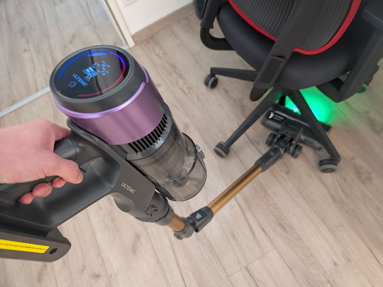 Eine Person hält einen kabellosen Staubsauger Ultenic U20 mit digitalem Display und reinigt in der Nähe eines Bürostuhls. Eine Person hält einen kabellosen Staubsauger Ultenic U20 mit digitalem Display und reinigt in der Nähe eines Bürostuhls.