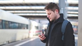 Mann mit Smartphone auf einem Bahnhof