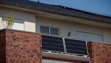 Ein Balkon mit Solarpanelen an einer Backsteinwand eines Hauses.
