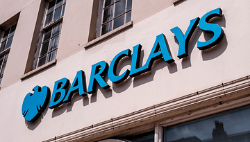 Ein Barclays-Schild mit einem blauen Logo an einer beigen Wand.