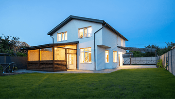 Ein modernes zweistöckiges Haus mit hellen Fenstern und einem Rasen im Dämmerlicht.