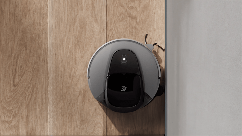 G10+ Saugroboter von 3i, in der Nähe einer Wand auf Holzboden positioniert. G10+ Saugroboter von 3i, in der Nähe einer Wand auf Holzboden positioniert.