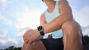Ein Mann mit einer Kospet P10-Smartwatch, der im Freien sitzt, mit blauem Himmel im Hintergrund.