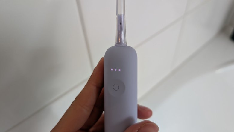 Eine Hand hält eine lila elektrische Zahnbürste mit einem klaren Kopf und drei Statusleuchten. Eine Hand hält eine lila elektrische Zahnbürste mit einem klaren Kopf und drei Statusleuchten.