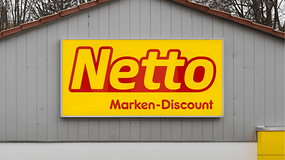 Netto Marken-Discount-Logo auf gelbem Hintergrund an einer grauen Wand angebracht.