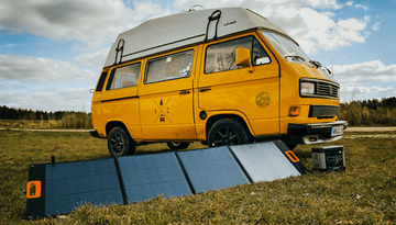 Ein gelber Campervan, der auf Gras steht, mit einem Solarpanel und einer Batterie davor.