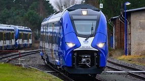 Ein blauer Wasserstoffzug auf Gleisen in Berlin, mit einem Stationsschild im Hintergrund.