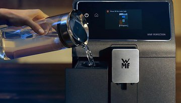 Eine Person gießt Wasser in eine WMF-Kaffeemaschine mit einem digitalen Display.