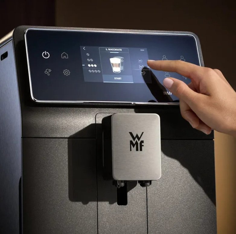Eine Person interagiert mit einer Touchscreen-Kaffeemaschine, die eine Macchiato-Option anzeigt. Eine Person interagiert mit einer Touchscreen-Kaffeemaschine, die eine Macchiato-Option anzeigt.