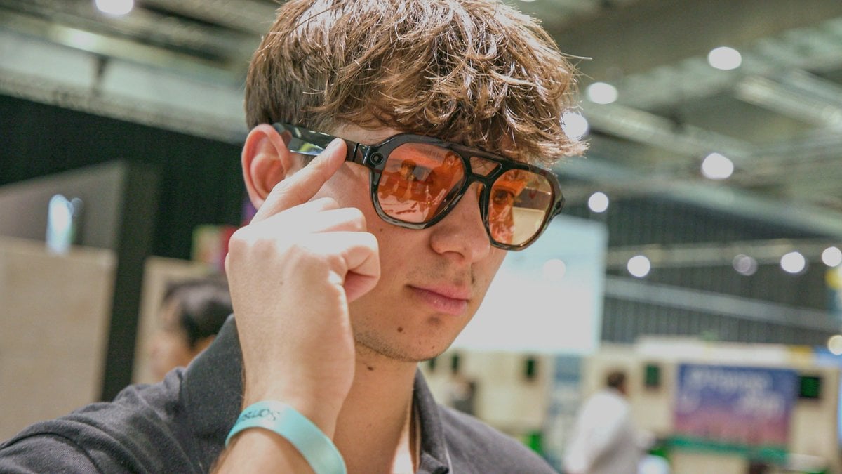 Un jeune homme portant des lunettes de soleil élégantes, se touchant la tempe, dans un espace intérieur.