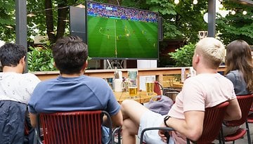 Gruppe von Freunden, die ein Fußballspiel auf einem Sylvox 4K Fernseher im Garten ansehen.