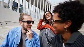 Drei Freunde lachen und tragen Sonnenbrillen bei einer Veranstaltung auf Stufen.