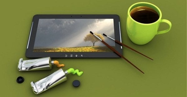 Tablette numérique avec une image de paysage, pinceaux, tubes de peinture et une tasse de café sur un fond vert.